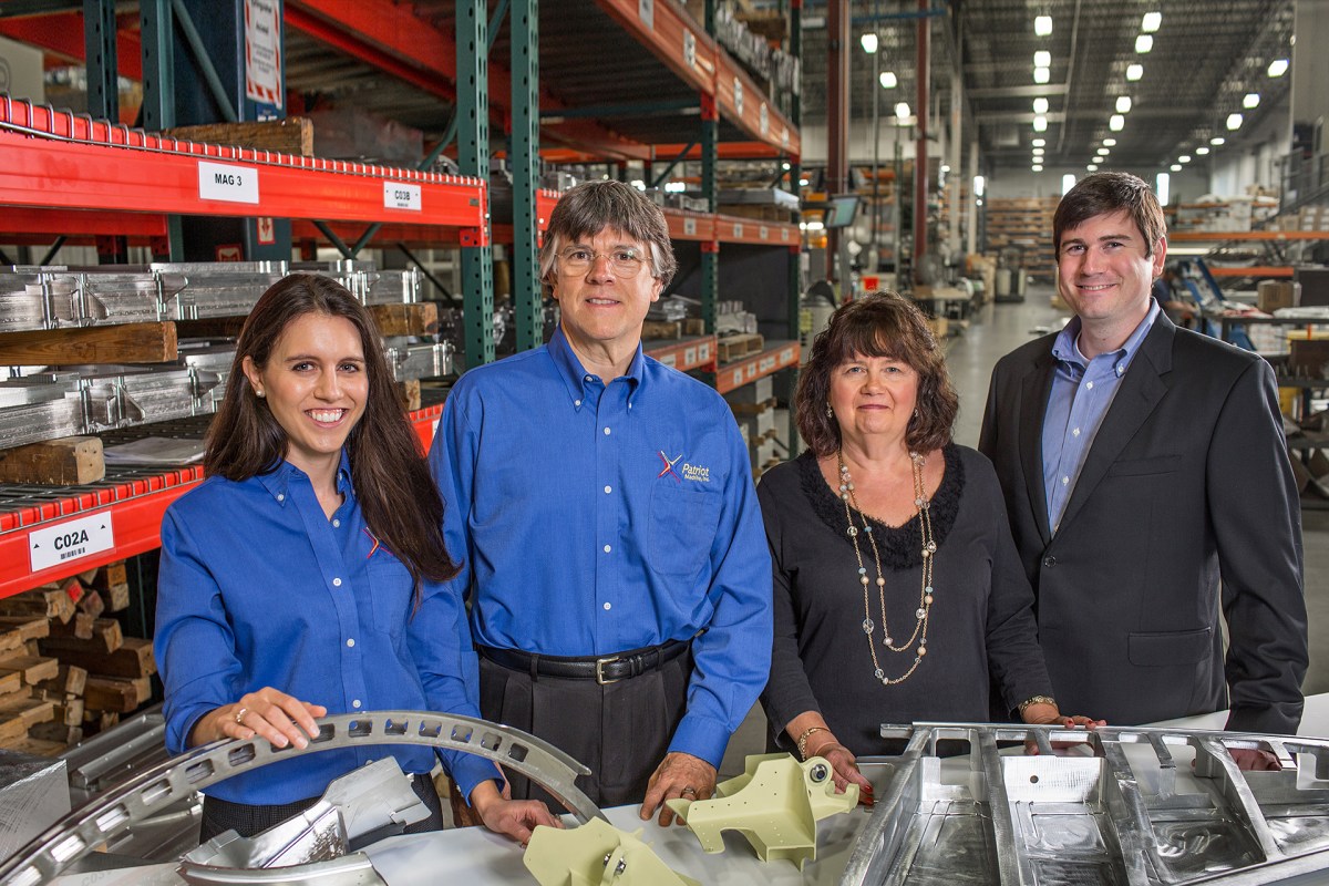 Four members of the Burns family on the shop floor, with machined parts visible in front of them.