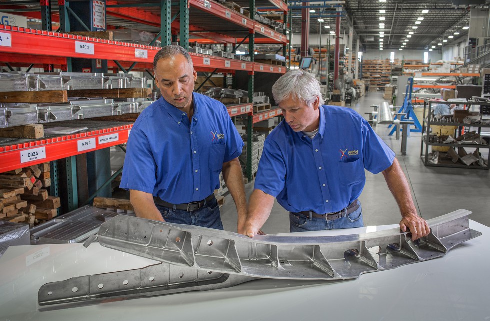 Two Patriot Machine associates examining a part on a table together.